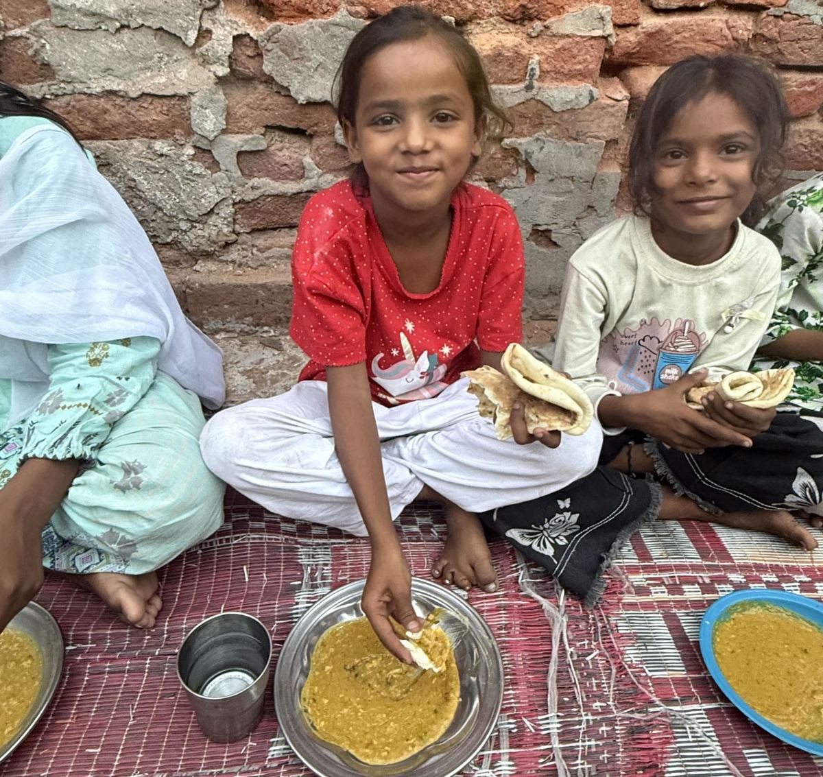 Deux fillettes souriantes mangent leur repas, assises par terre