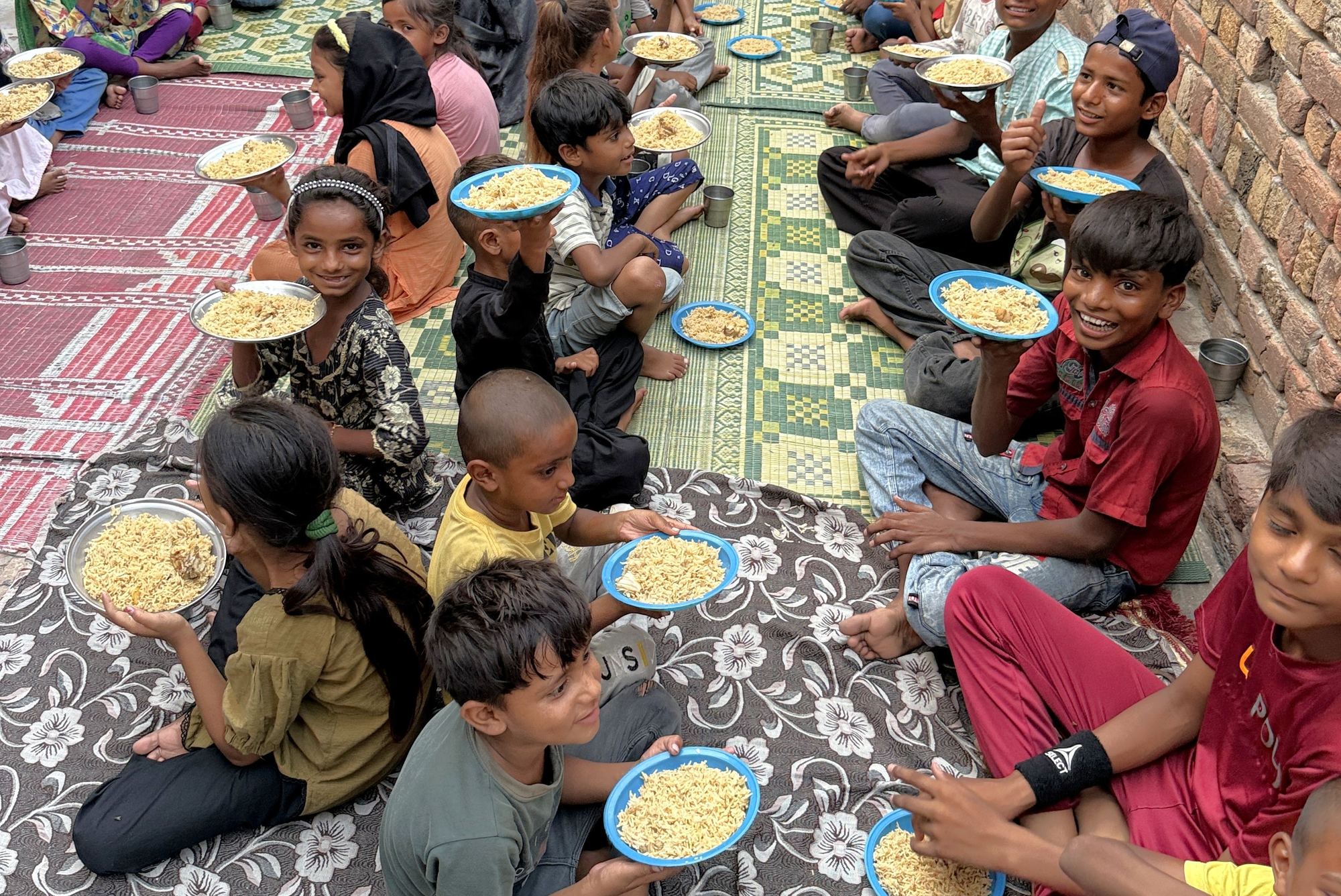 Des orphelins souriants, assis par terre, montrent leur assiette de nourriture