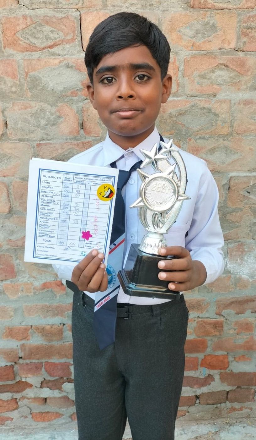 Nehemia, en uniforme scolaire, tient fièrement son trophée et son bulletin